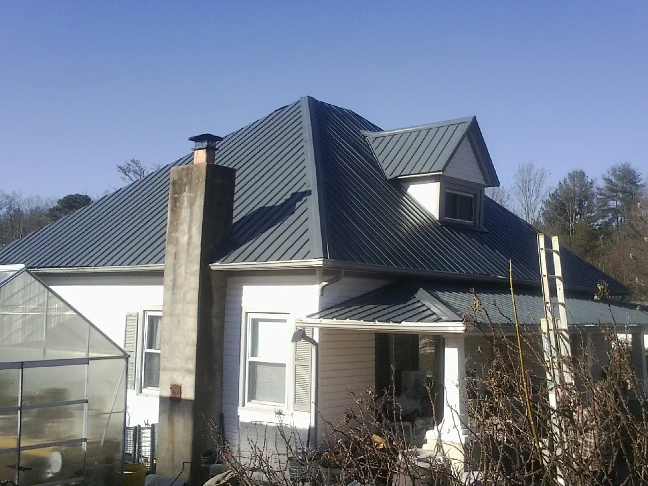 Dark blue standing seam metal roof on a white farmhouse with dormer — Slate & Tile Roof Repair by Roofing Brothers in Alleman