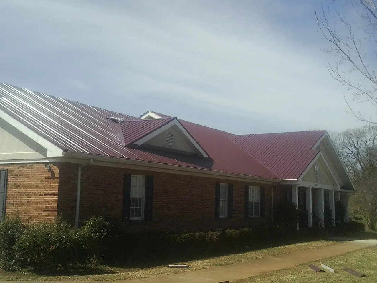 Red metal roof with gabled entries on a long brick building, from a Hail Damage Roof Repair job in Alleman