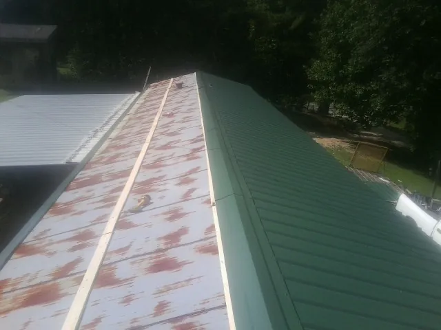 Old rusted panels beside newly installed green metal roofing — Wind Damage Roof Repair by Roofing Brothers in Alleman
