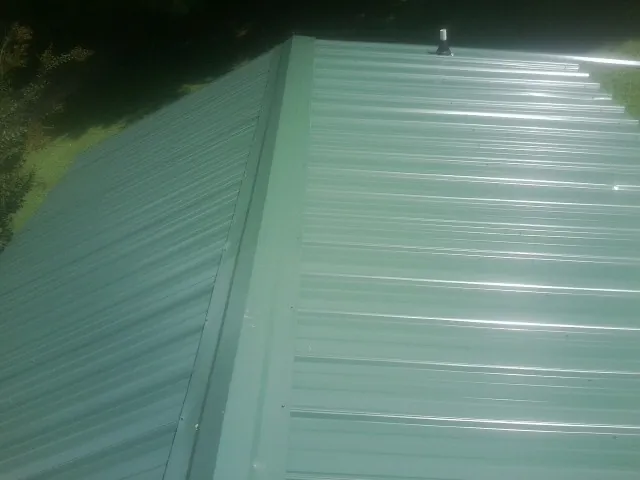 New green metal panels meeting at the ridge of a roof — Flat Roof Repair work by our crew in Alleman