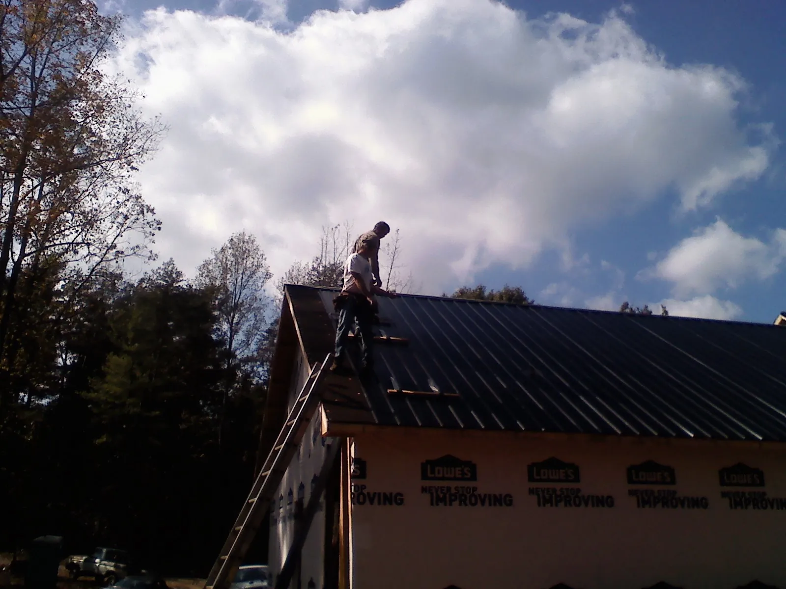 Roofer fastening dark metal panels high against a cloudy sky, from a Roof Inspection job in Alleman