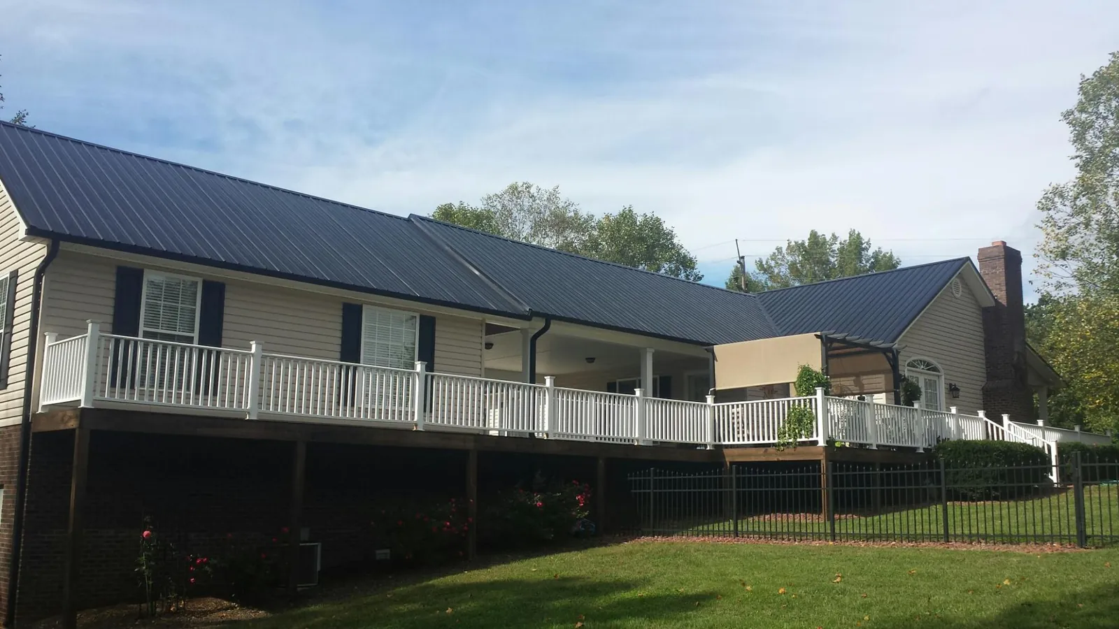 Black metal roof above a long white railed deck on a hillside home in Alleman