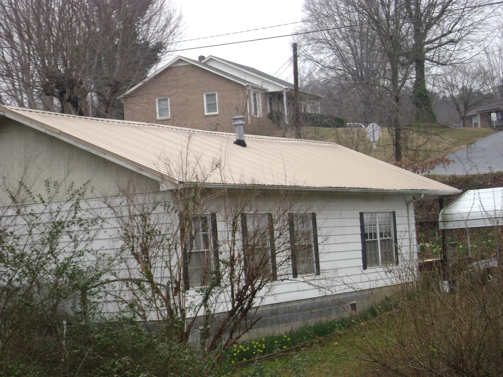Tan metal roof on a white sided house set into a hillside — Commercial Roofing by Roofing Brothers in Alleman