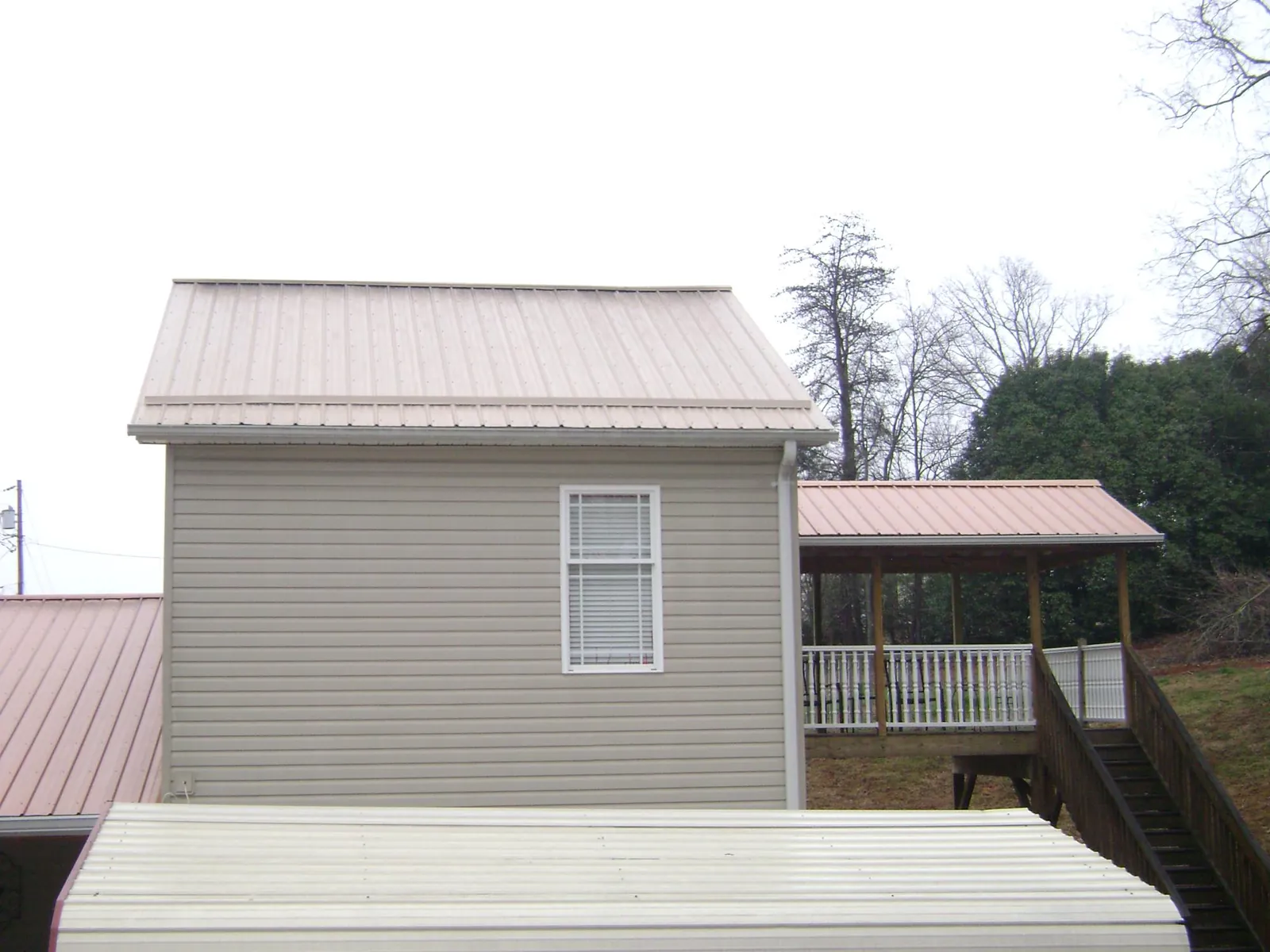 Tan metal roofs on a two story addition and attached porch, from a Roof Replacement job in Alleman